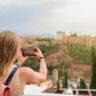 Young blonde female tourist taking the picture of Alhambra in Granada, Spain