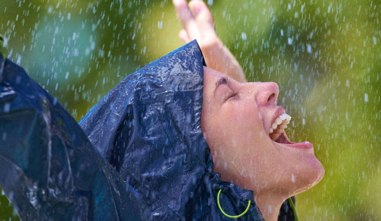 Cropped shot of a young woman standing happily in the rain in her raincoat
