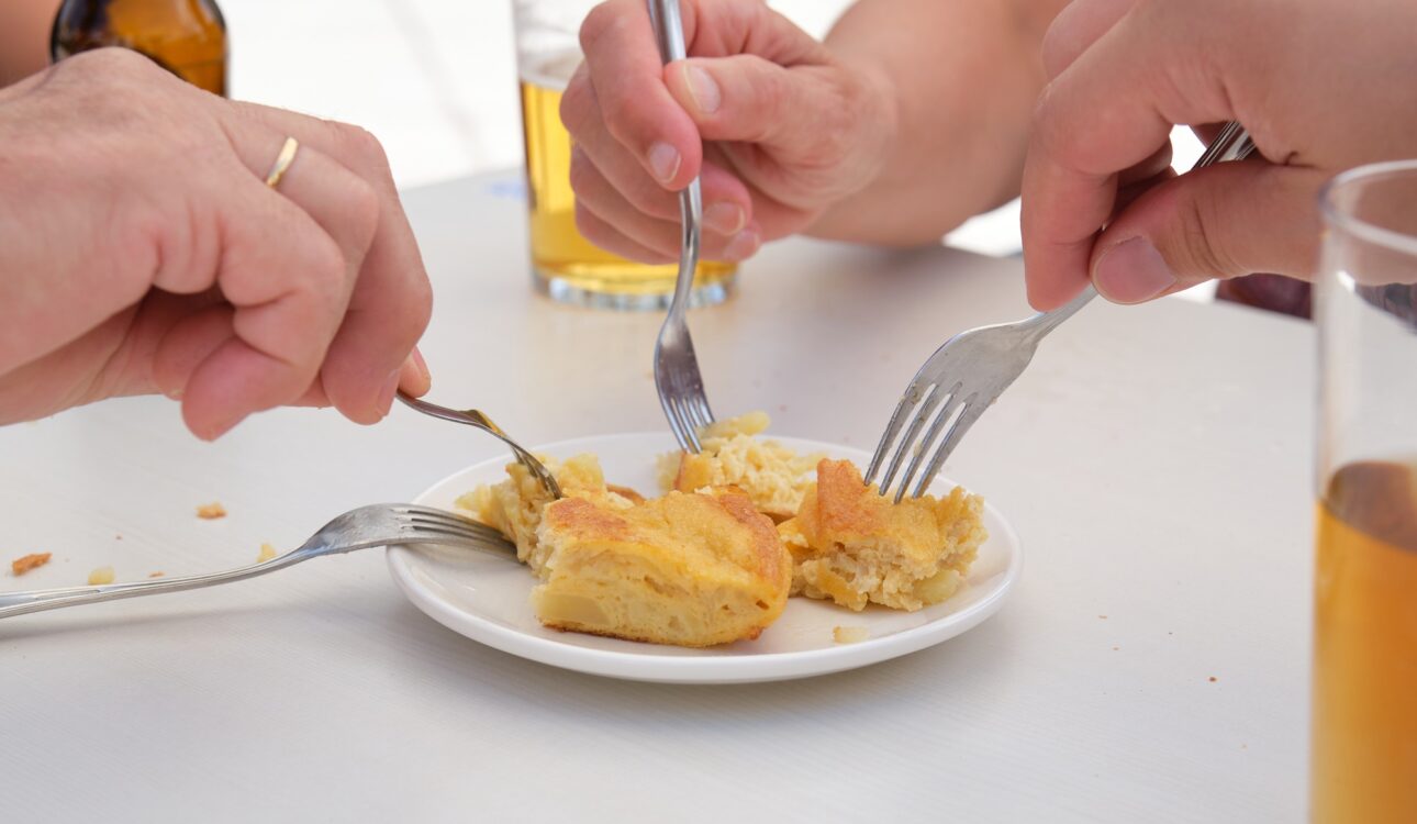 Group of people sharing a piece of Spanish omelette and drinking beer.