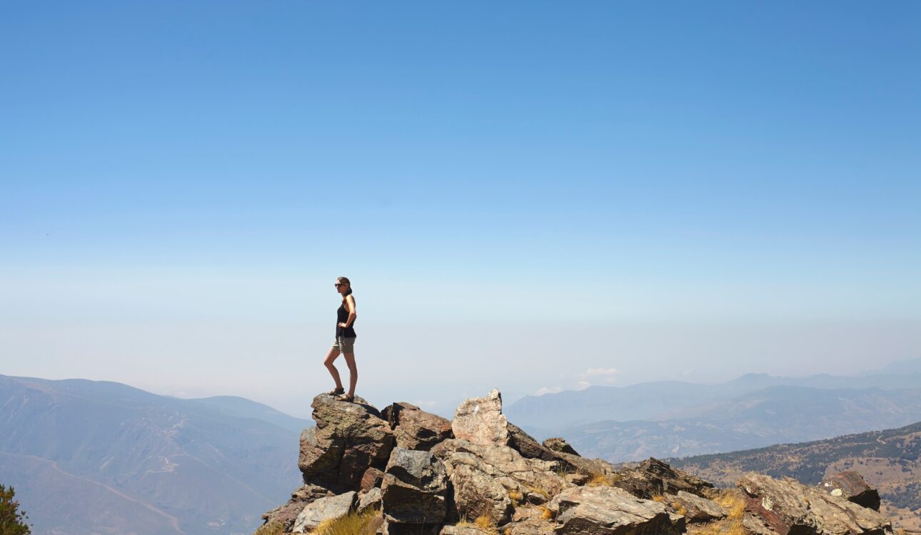 Young woman standing on top of rocks gazing at view, Sierra Nevada, Andalucia Granada, Spain