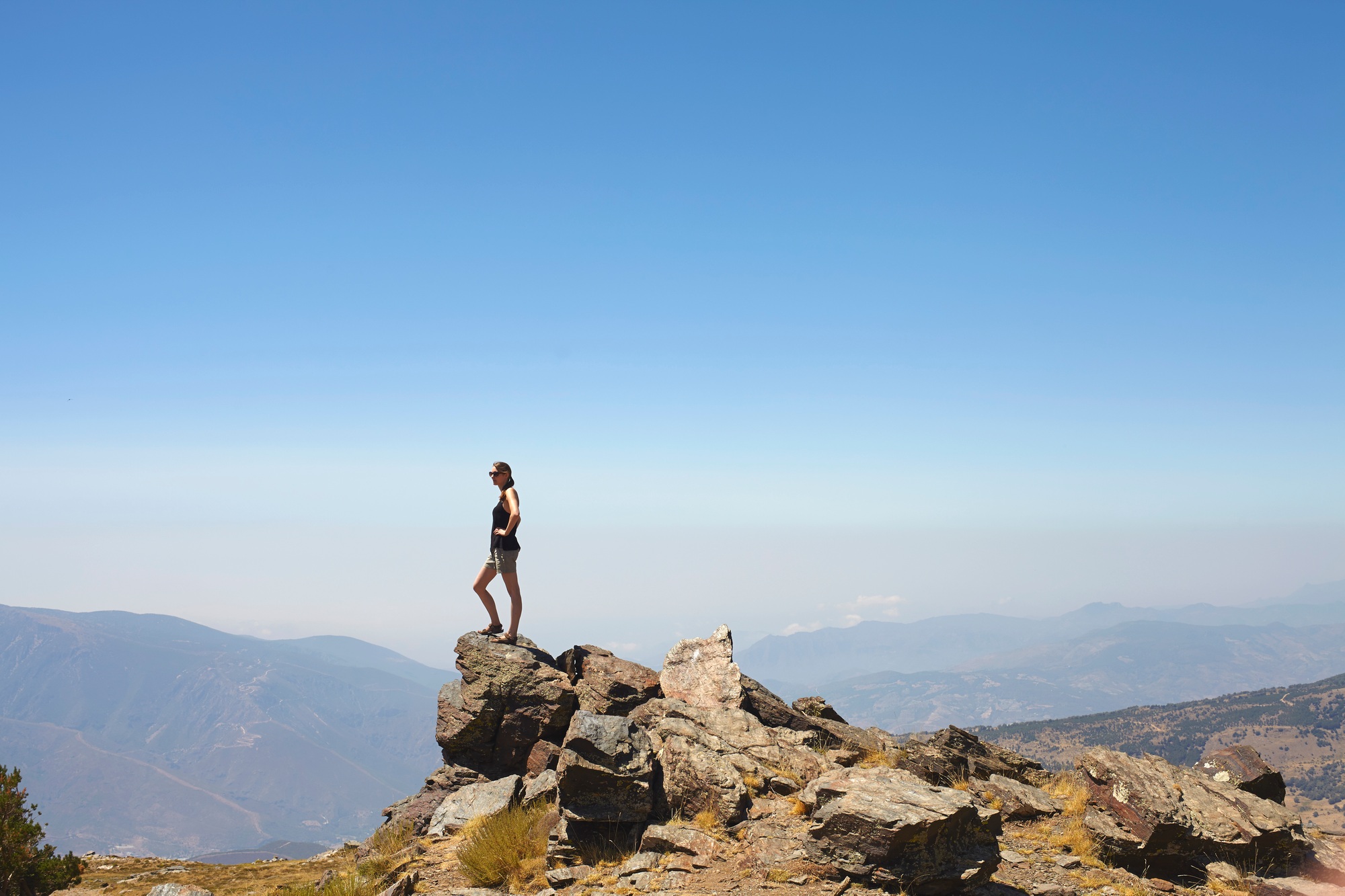 Young woman standing on top of rocks gazing at view, Sierra Nevada, Andalucia Granada, Spain