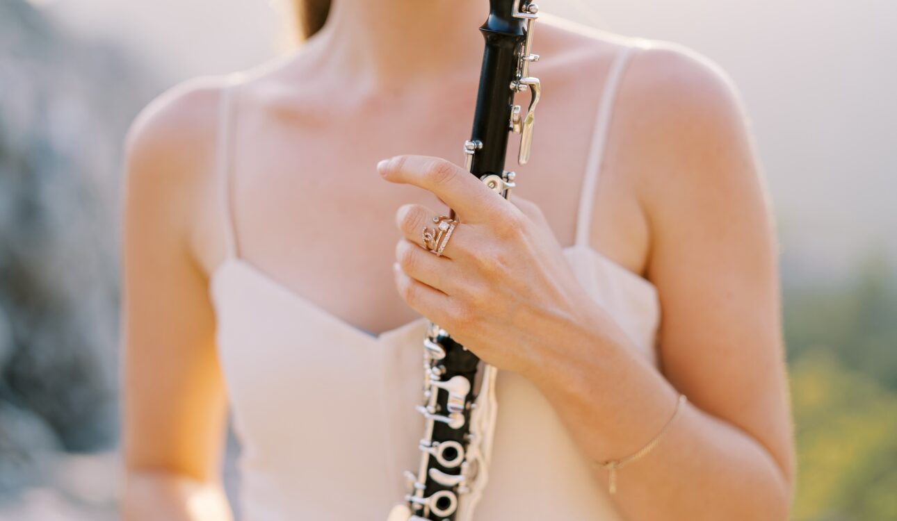 Girl musician plays the clarinet while standing in the mountains. Cropped. Faceless
